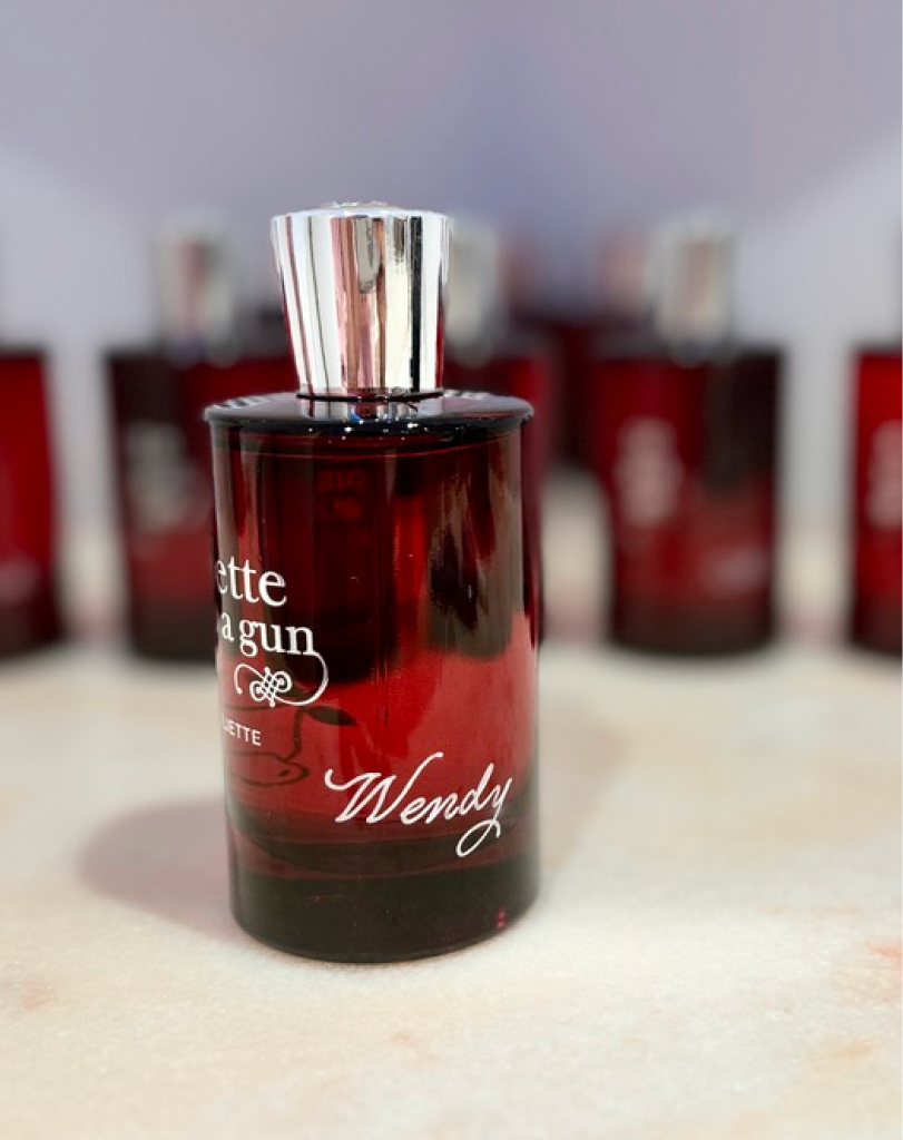 A close-up shot of a dark red 'Juliette Has a Gun' perfume bottle with a silver cap, featuring the personalized name 'Wendy' engraved in white script on the front.