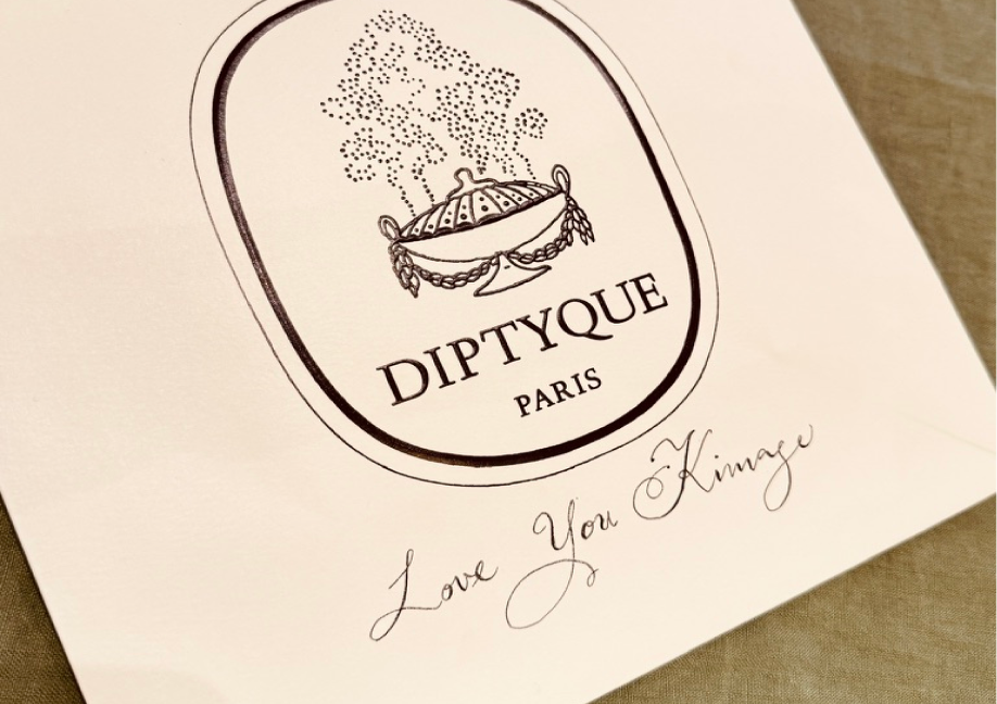 A detailed close-up of the Diptyque Paris oval logo on a white surface, featuring an illustration of a smoking incense burner. Below the logo, the words "Love You Kimaye" are elegantly written in black cursive calligraphy.