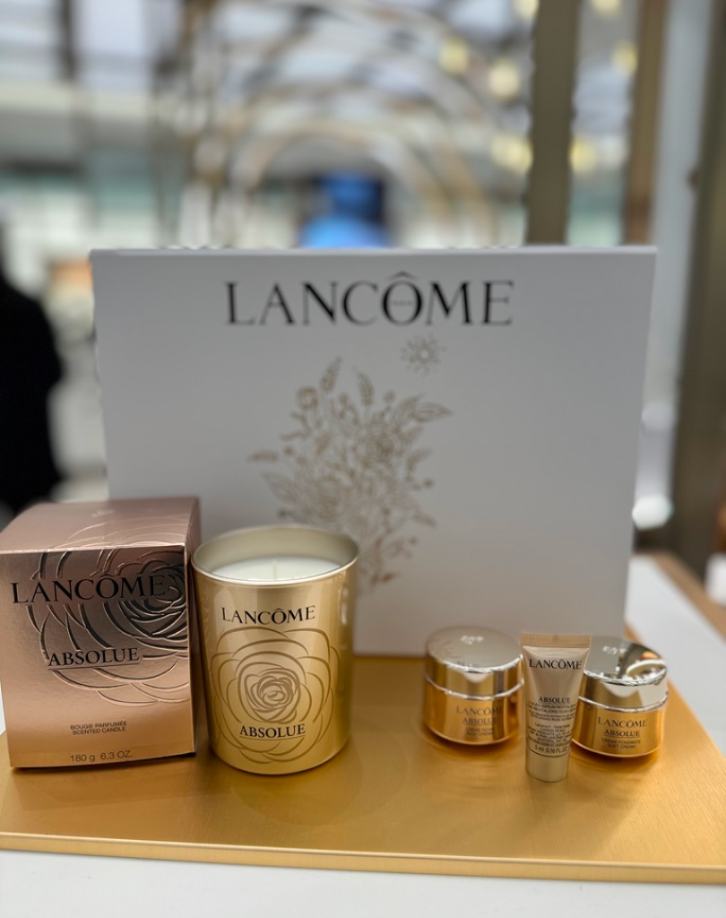 A Lancôme Absolue luxury gift set featuring a white branded box, a gold-cased scented candle, and various miniature skincare jars and tubes of the Absolue collection.