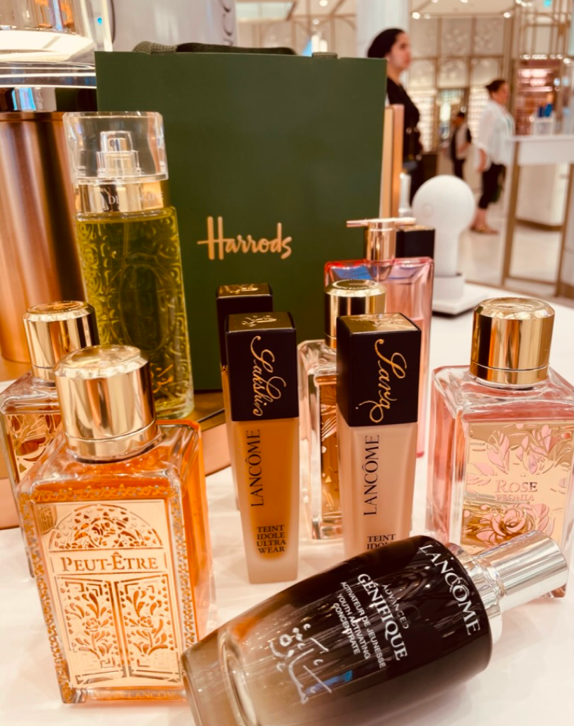 A variety of Lancôme luxury products including Maison Lancôme 'Peut-Être' and 'Rose Peonia' perfumes, alongside Teint Idole Ultra Wear foundation bottles, set against a green Harrods gift box.