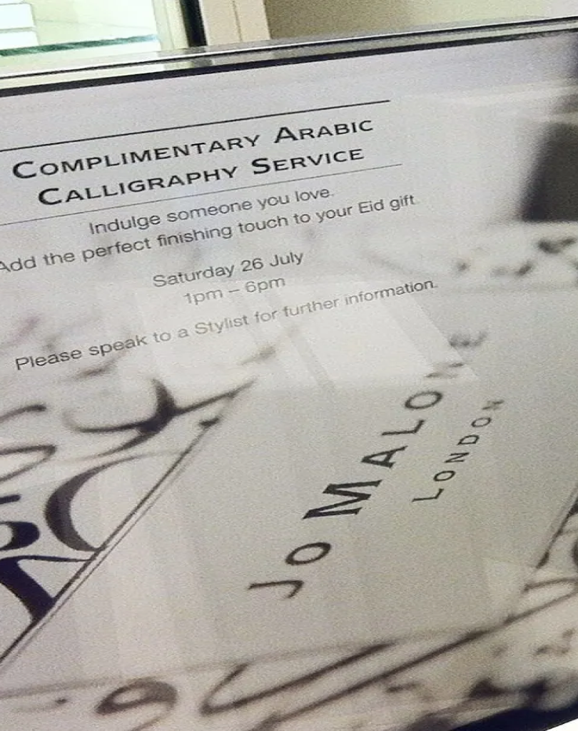 A close-up of a promotional sign for a "Complimentary Arabic Calligraphy Service" at Jo Malone London. The sign invites customers to add a finishing touch to Eid gifts and lists the service time as Saturday, 26 July, from 1pm – 6pm.