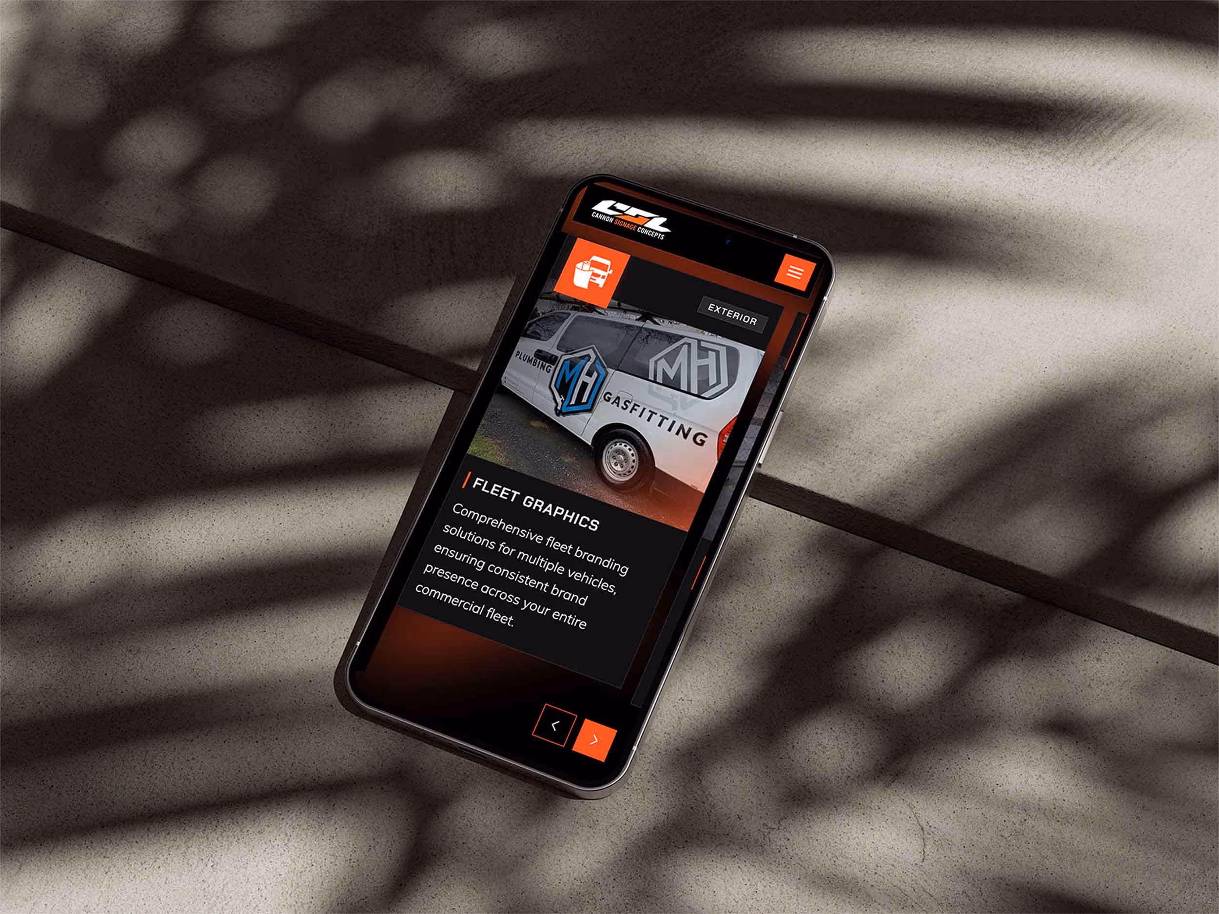 Smartphone on a textured surface displaying a webpage about fleet graphics featuring a van with MH Gasfitting branding.
