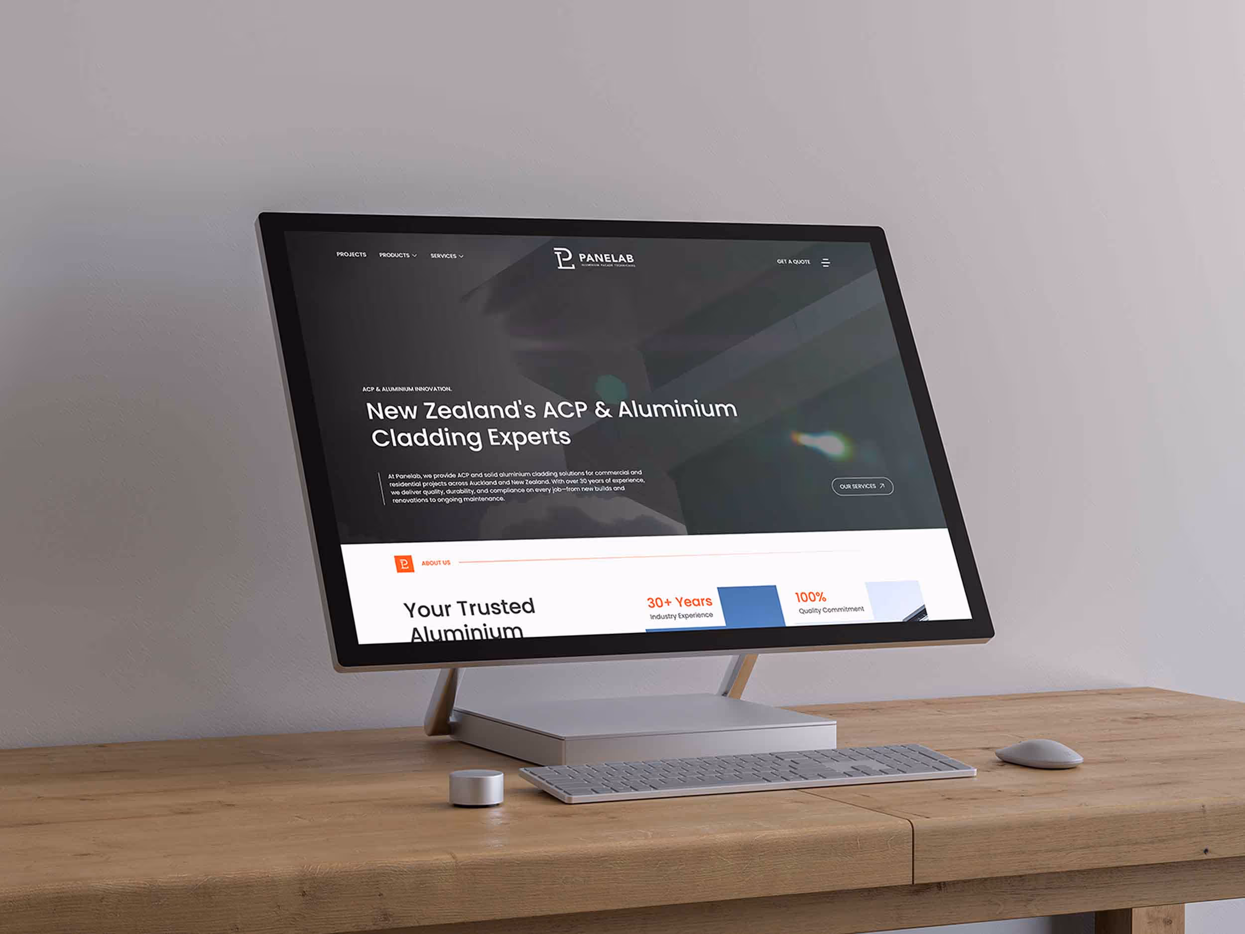Modern desktop computer on wooden table displaying a website for New Zealand's ACP and Aluminium cladding experts.