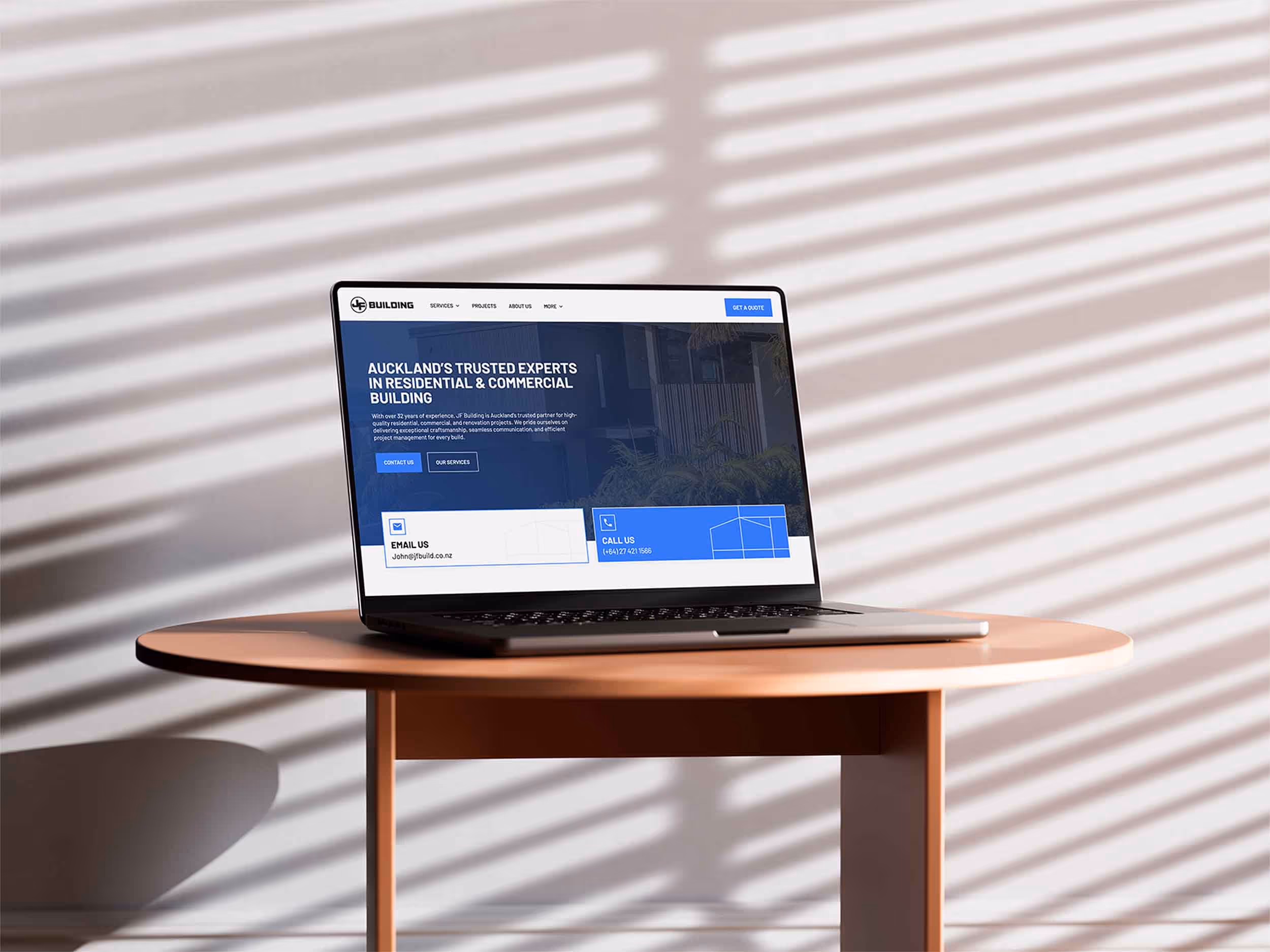 Laptop on a round table showing a website for Auckland residential and commercial building services with contact options.