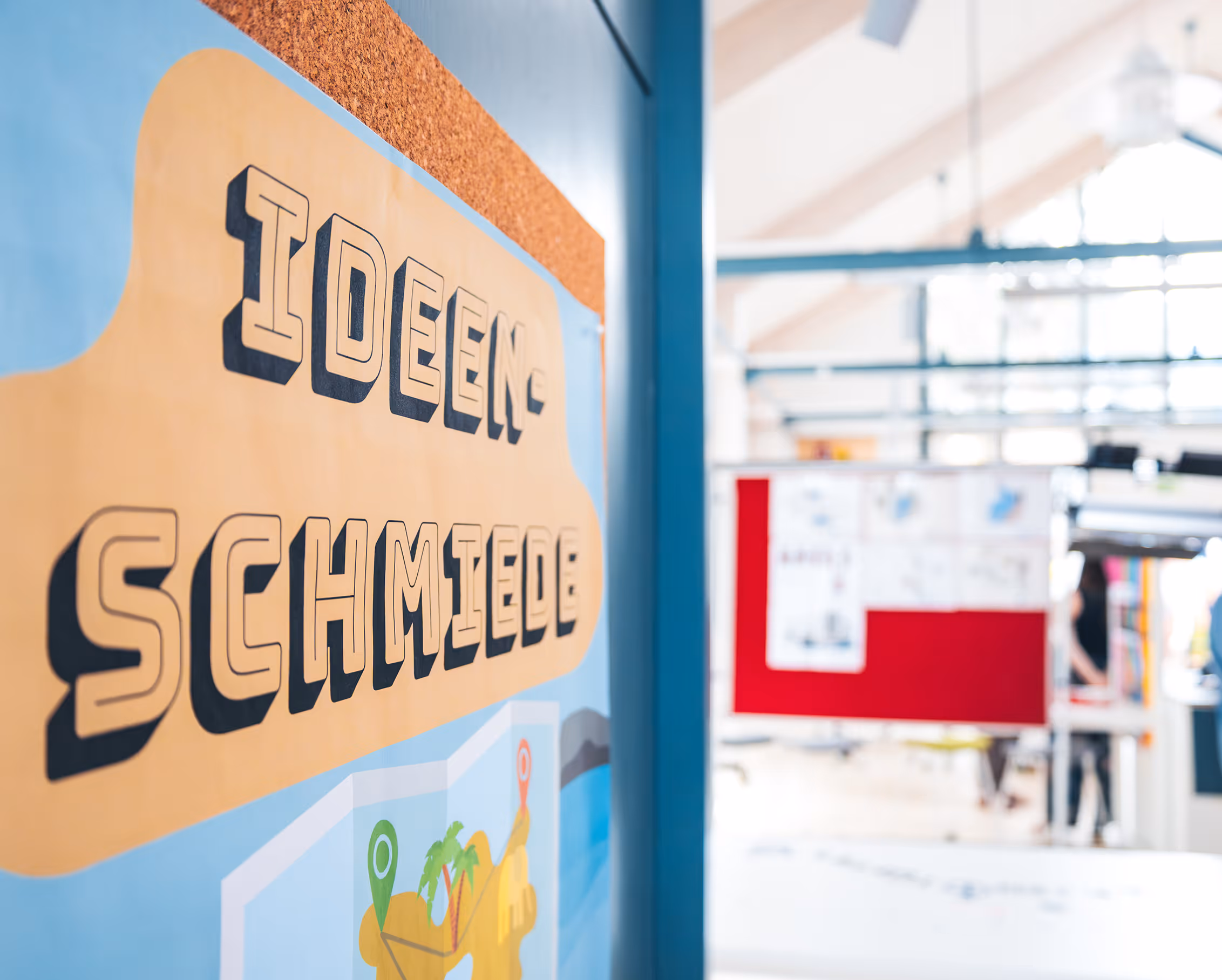 Eine bunte Wand mit der Aufschrift 'Ideenschmiede' und einer Karte mit Markierungen in einem modernen, hellen Büro.