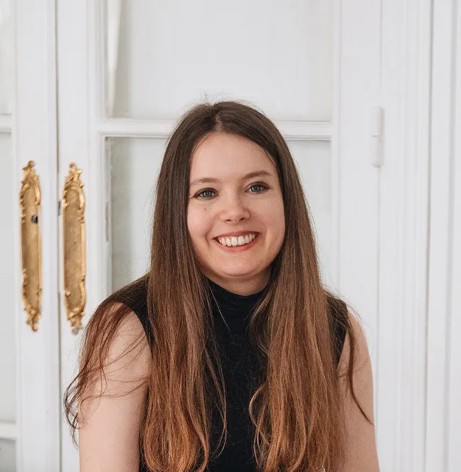 Smiling woman with long brown hair wearing a sleeveless black top in front of white doors with gold handles.