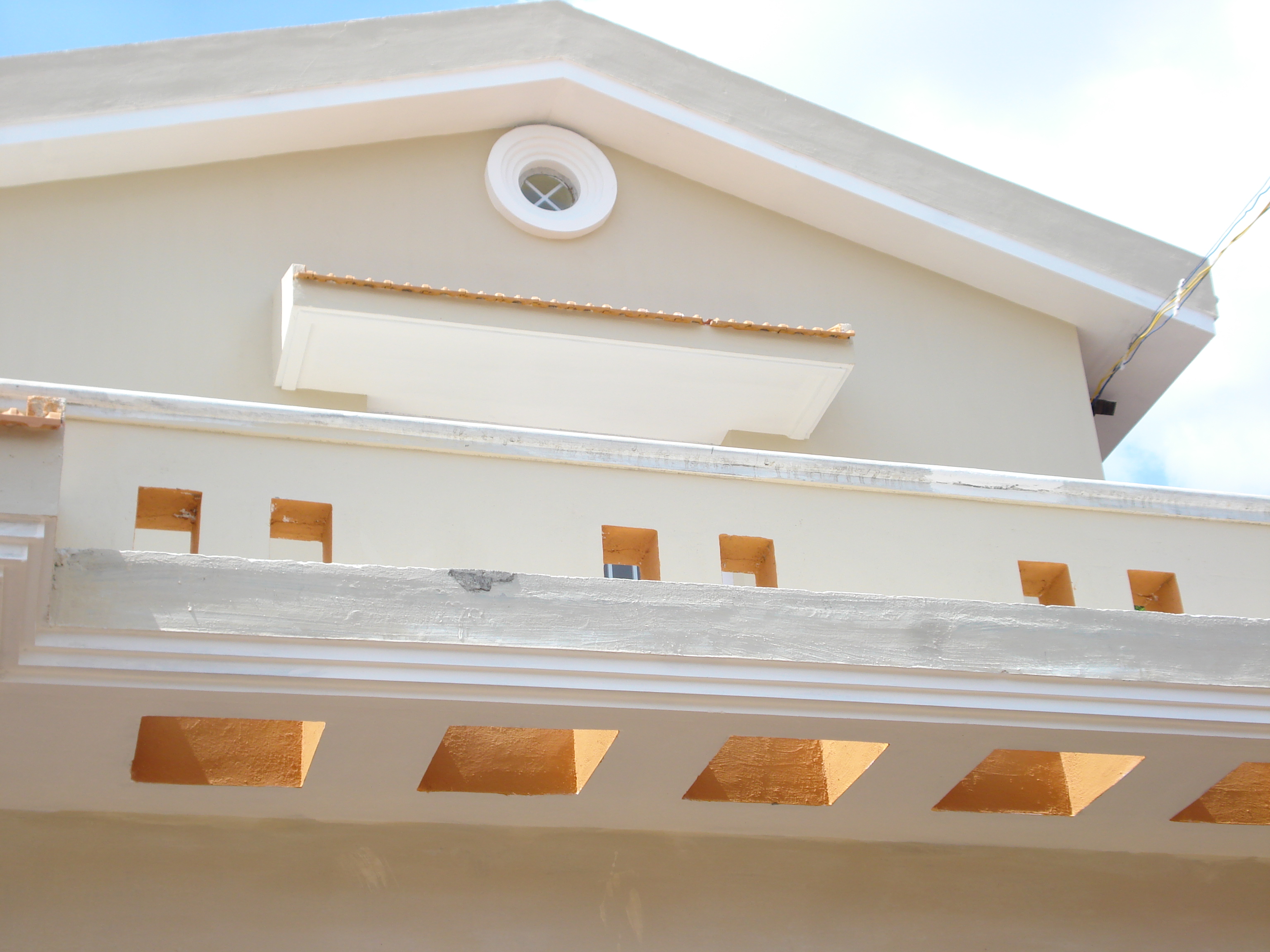 Upper facade of a beige building with rectangular cutouts and a small round window near the roof.