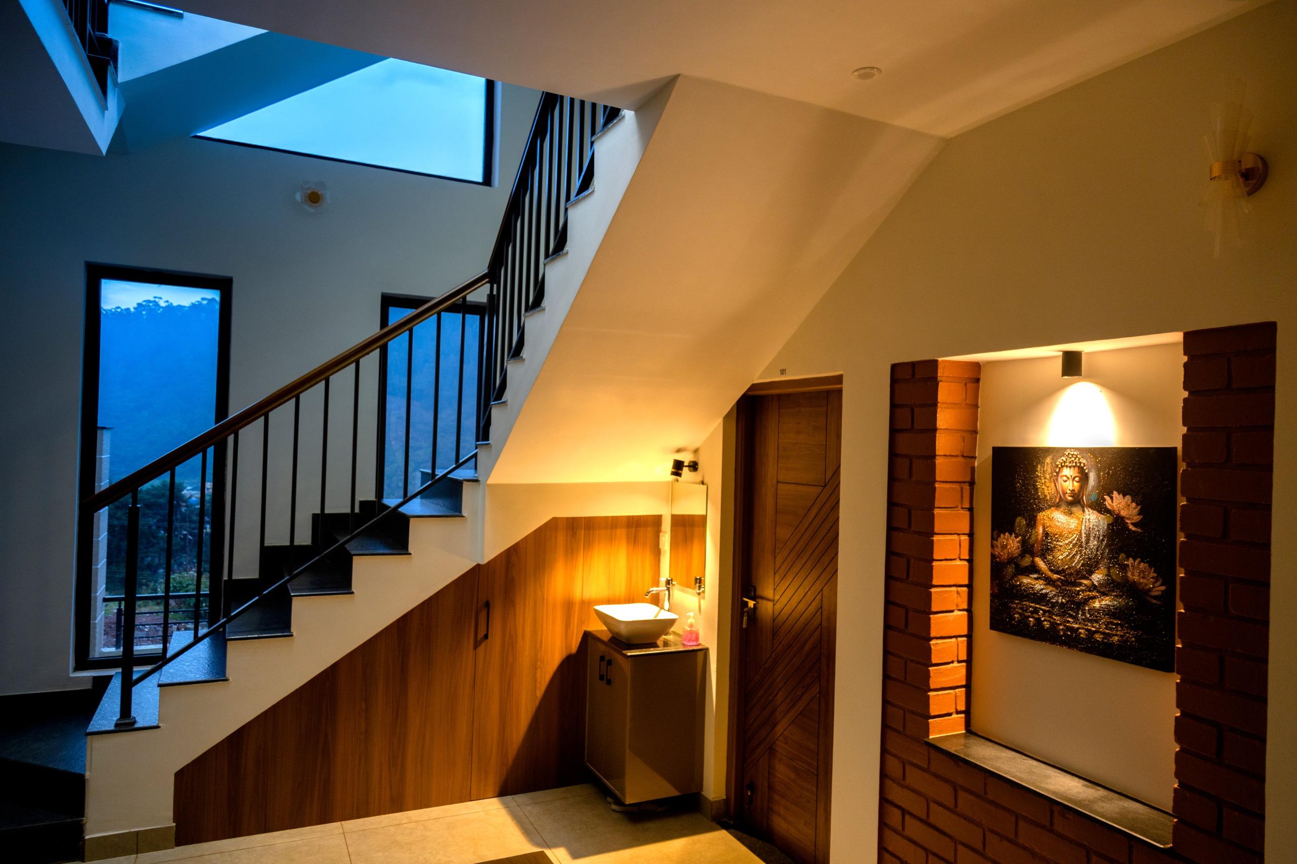 Indoor staircase with black metal railing next to a wooden cabinet with a sink and a lit Buddha painting on a brick inset wall.