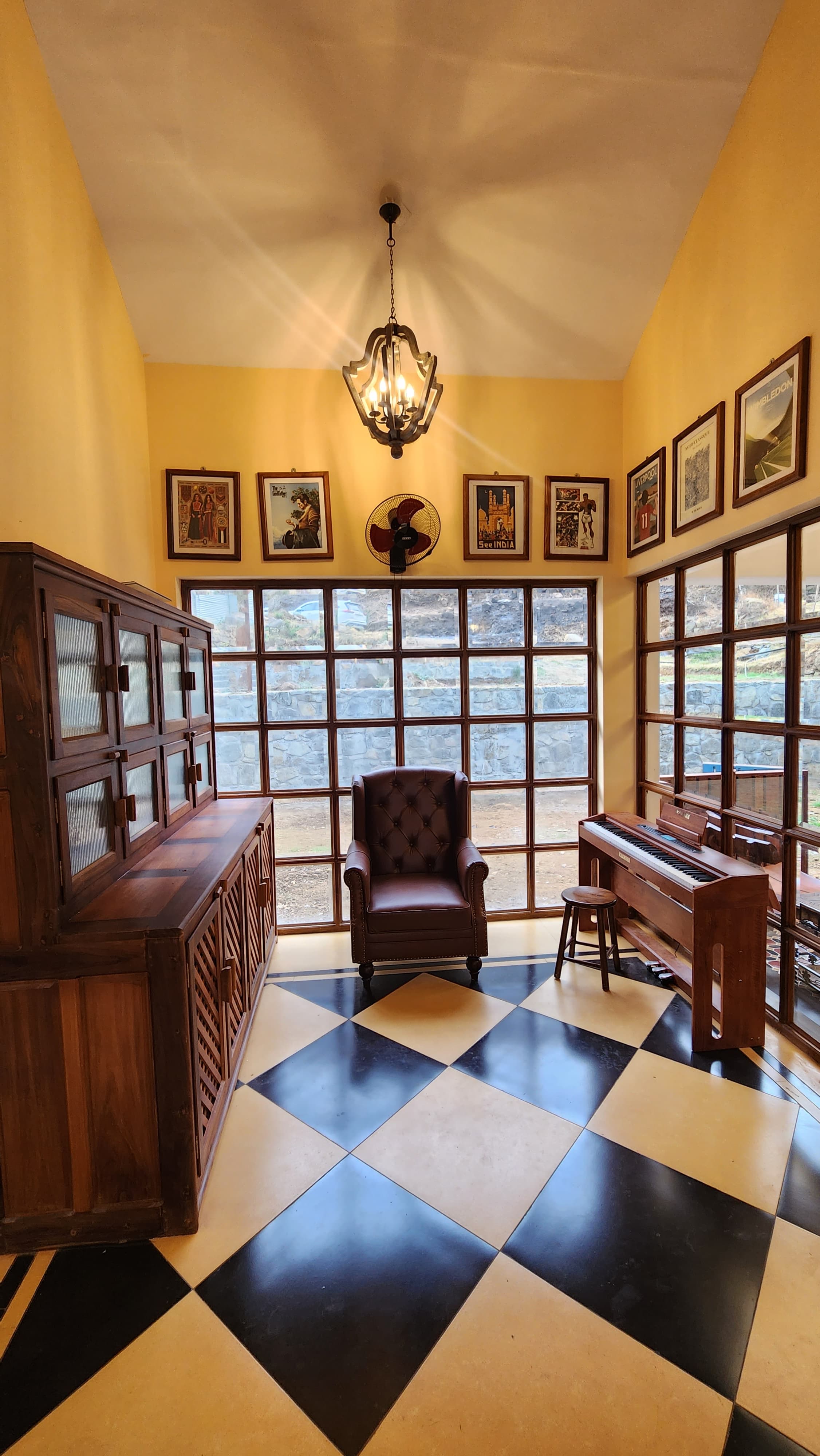 Room with yellow walls, checkered black and beige floor, brown leather armchair centered by large window, wooden cabinet on left, and wooden piano with stool on right.