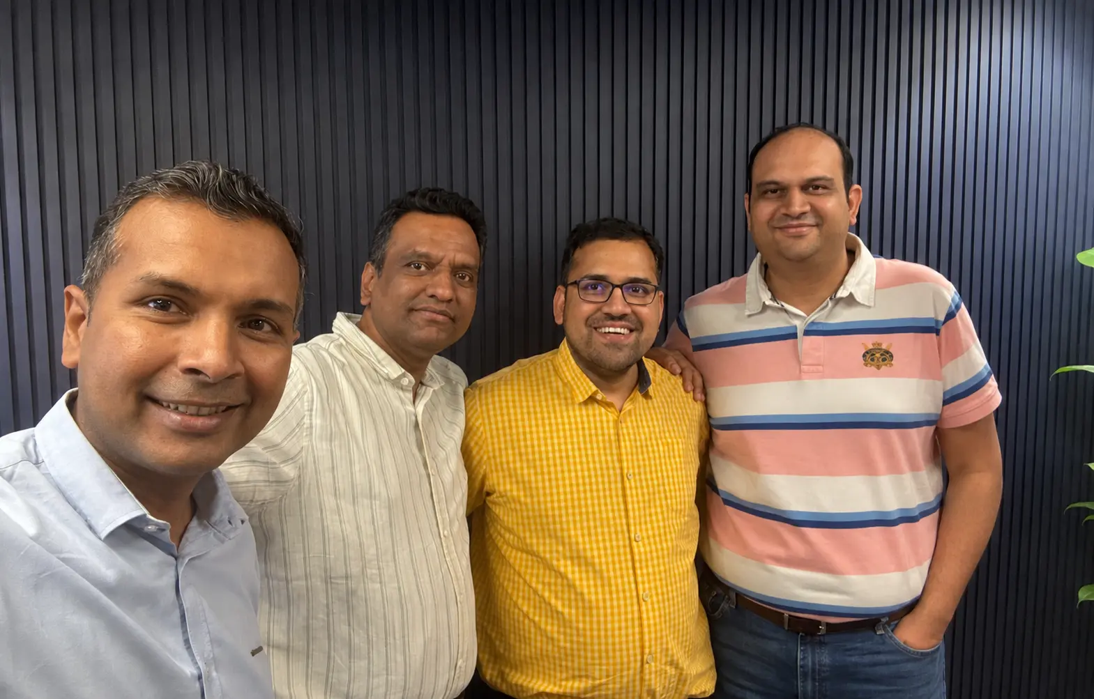 Four FreightFox team members smiling together for a group selfie against a dark ribbed wall