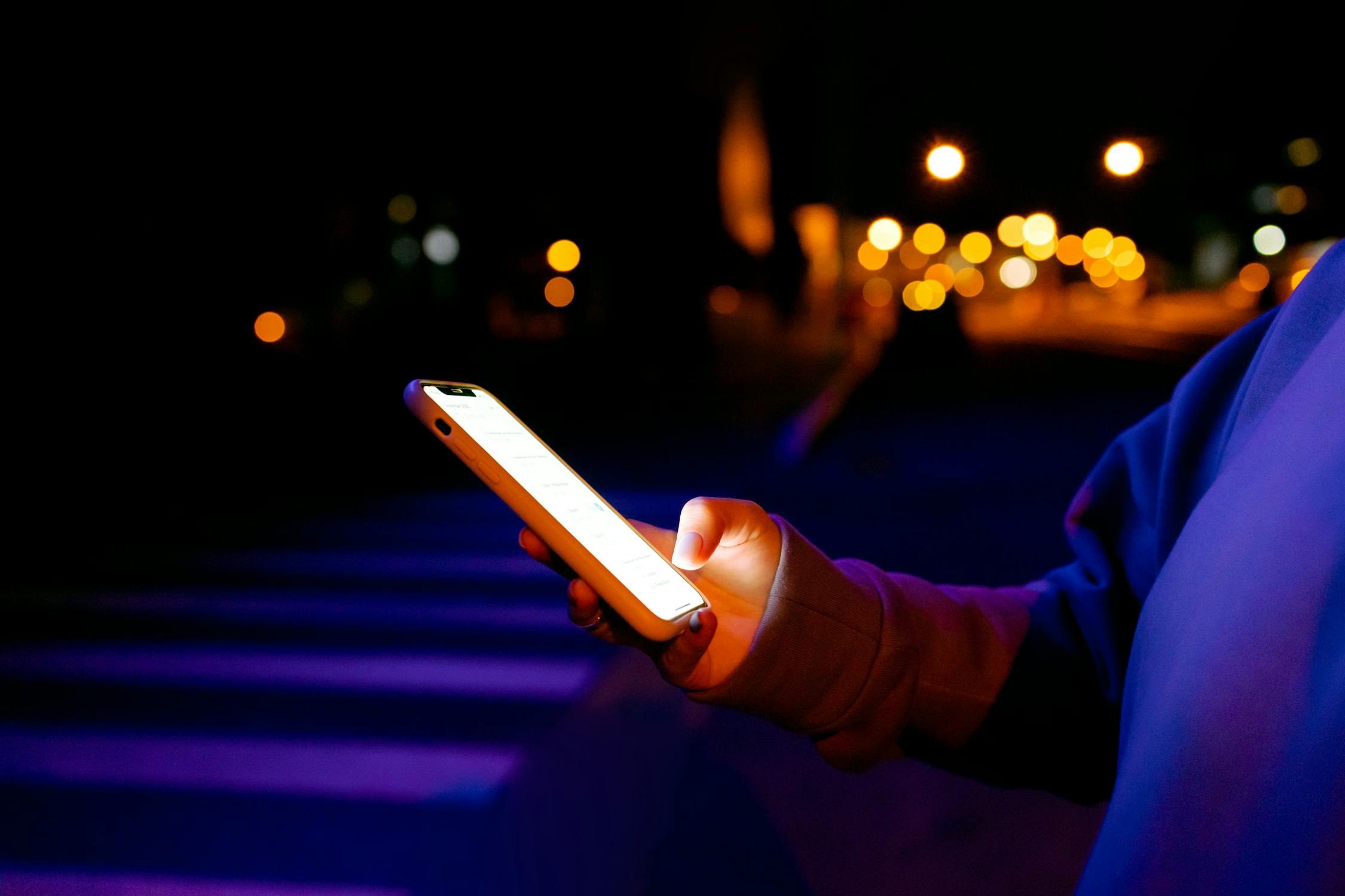 Person holding glowing smartphone at night with bokeh lights