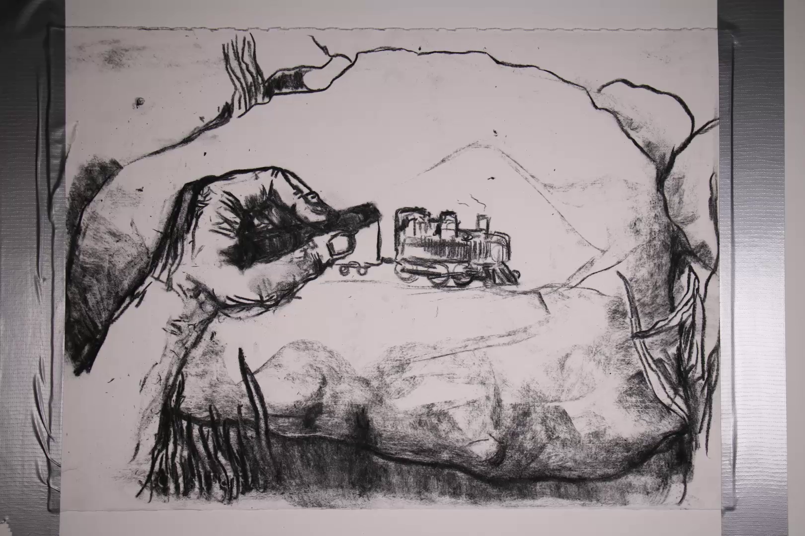 Black and white sketch of a hand drawing a small steam train on rocky terrain.