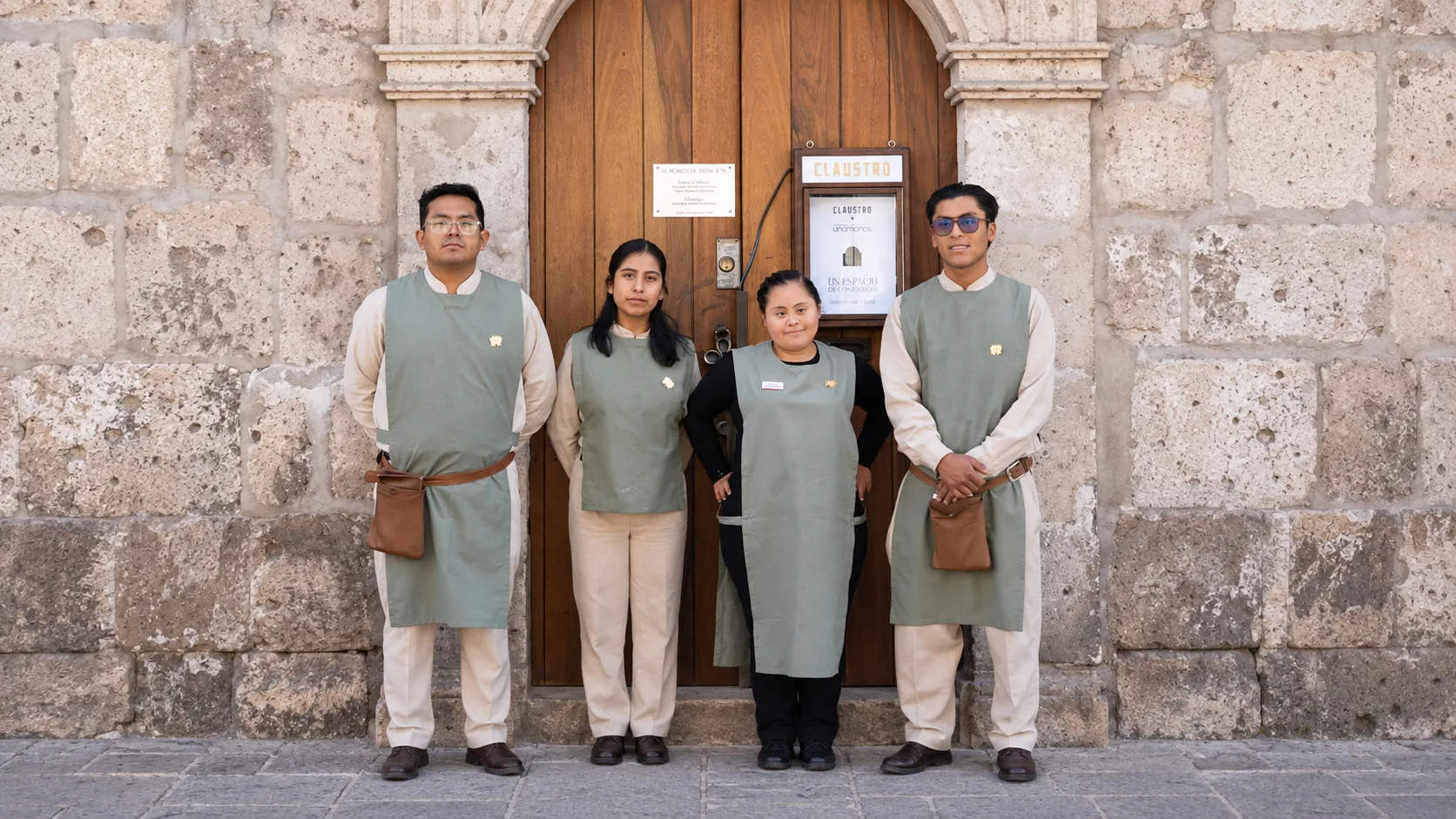 Vier Mitarbeitende des Claustro in Arequipa in grünen Schürzen vor der Holztür des Restaurants