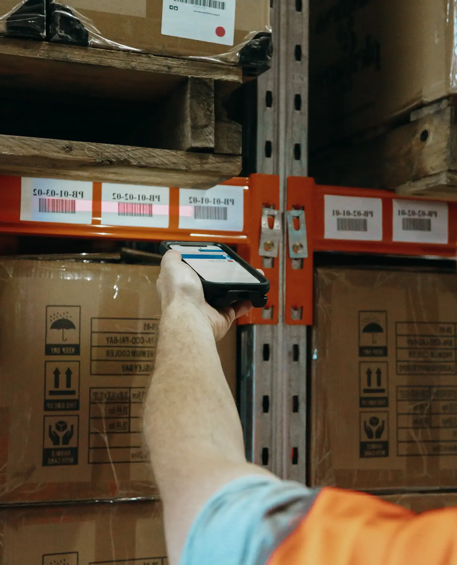 Person in an orange vest scanning barcode labels on warehouse shelves using a handheld device.