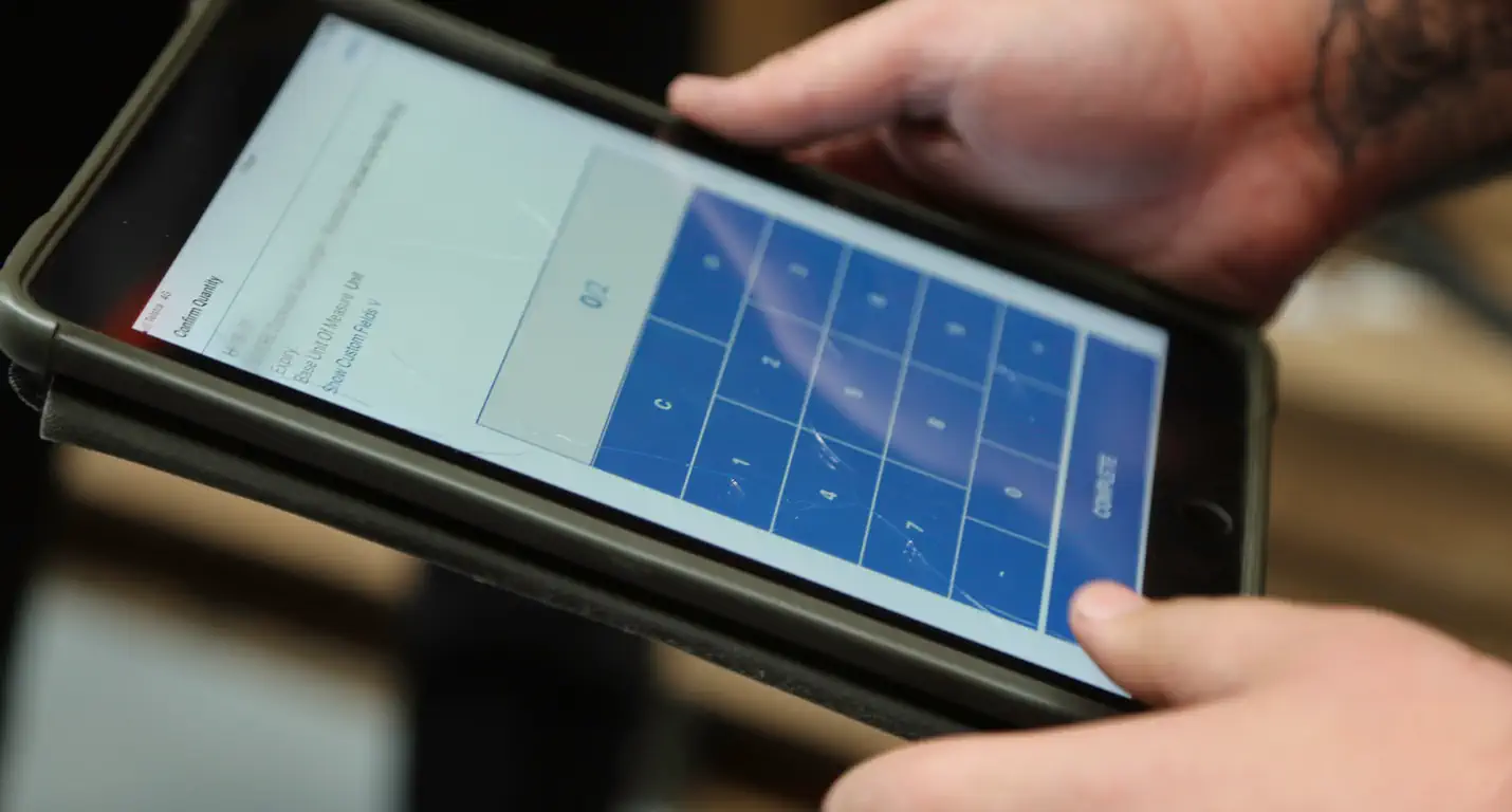 Hands holding a tablet displaying a numeric keypad and a quantity entry interface.