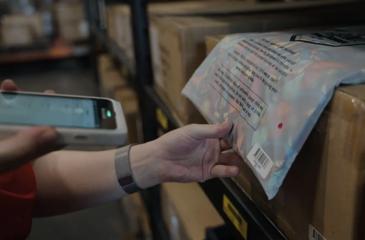 Person scanning a packaged product's barcode on a warehouse shelf using a handheld scanner.