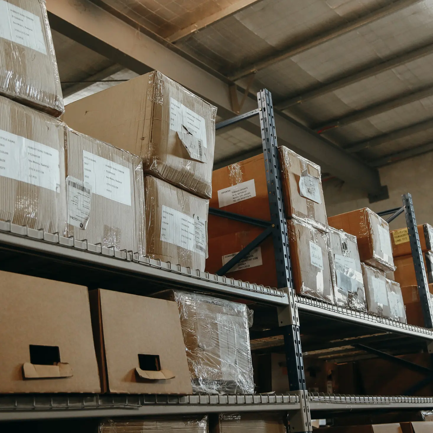 Warehouse metal shelves stacked with various cardboard boxes wrapped in plastic and labeled.
