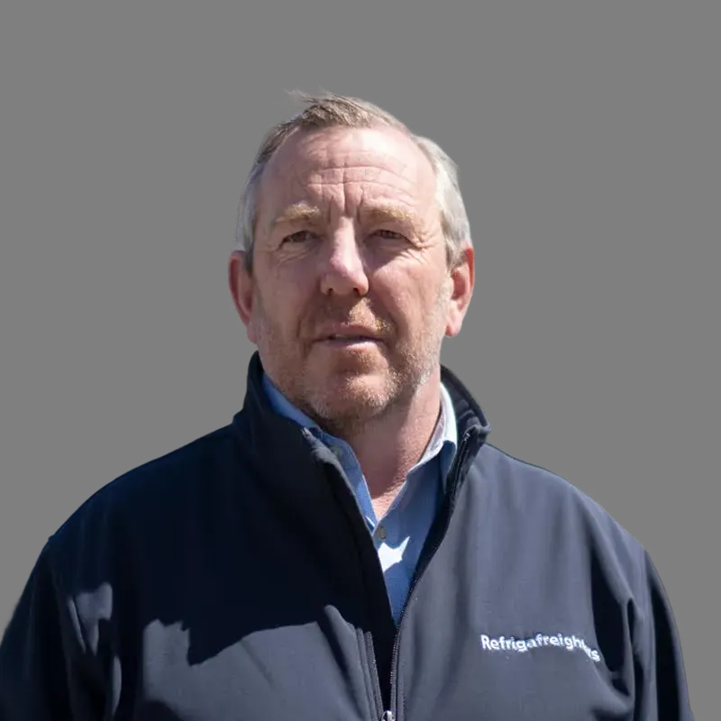 Middle-aged man with light hair wearing a navy jacket over a light blue collared shirt against a black background.