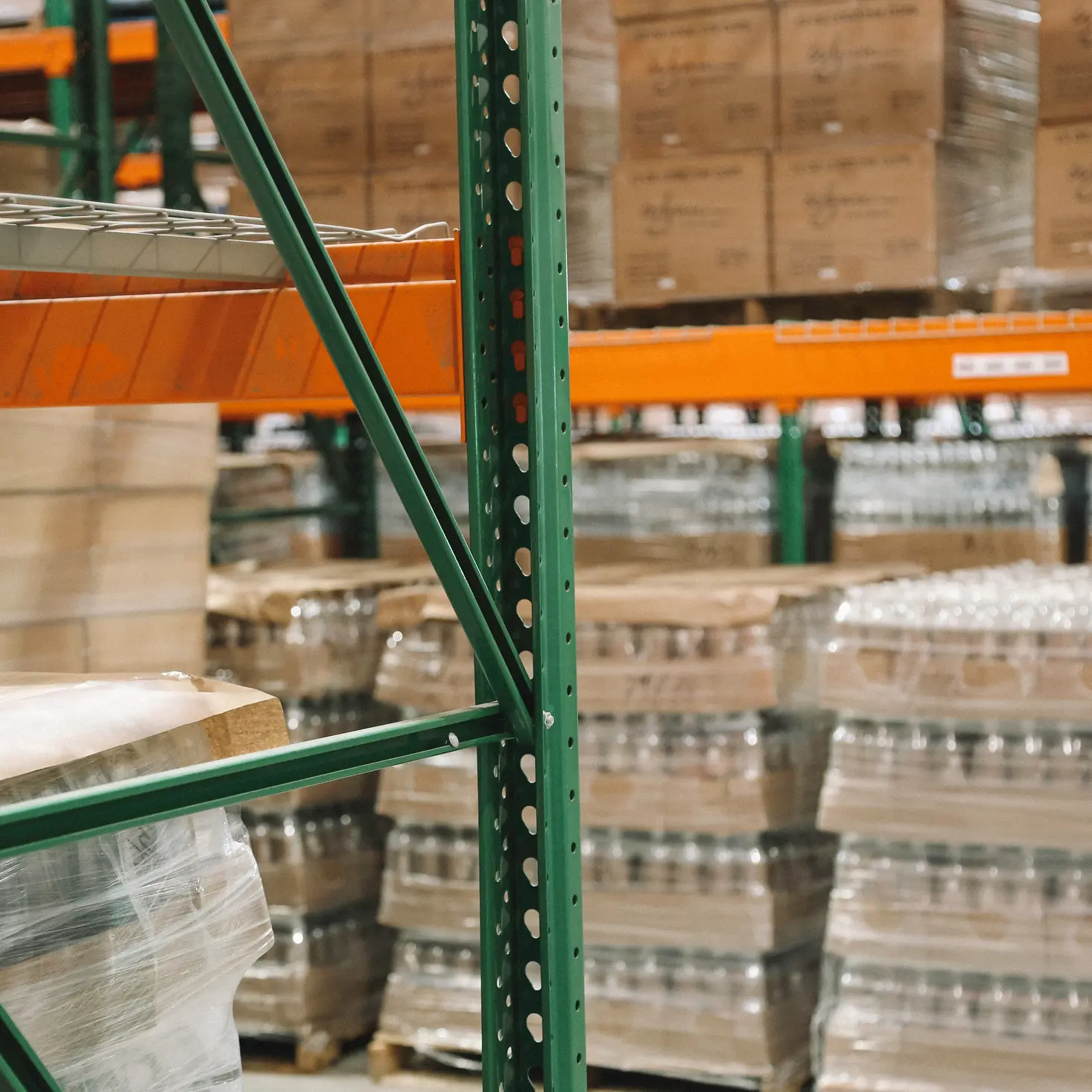 Warehouse shelves with stacked pallets wrapped in plastic containing boxed items.