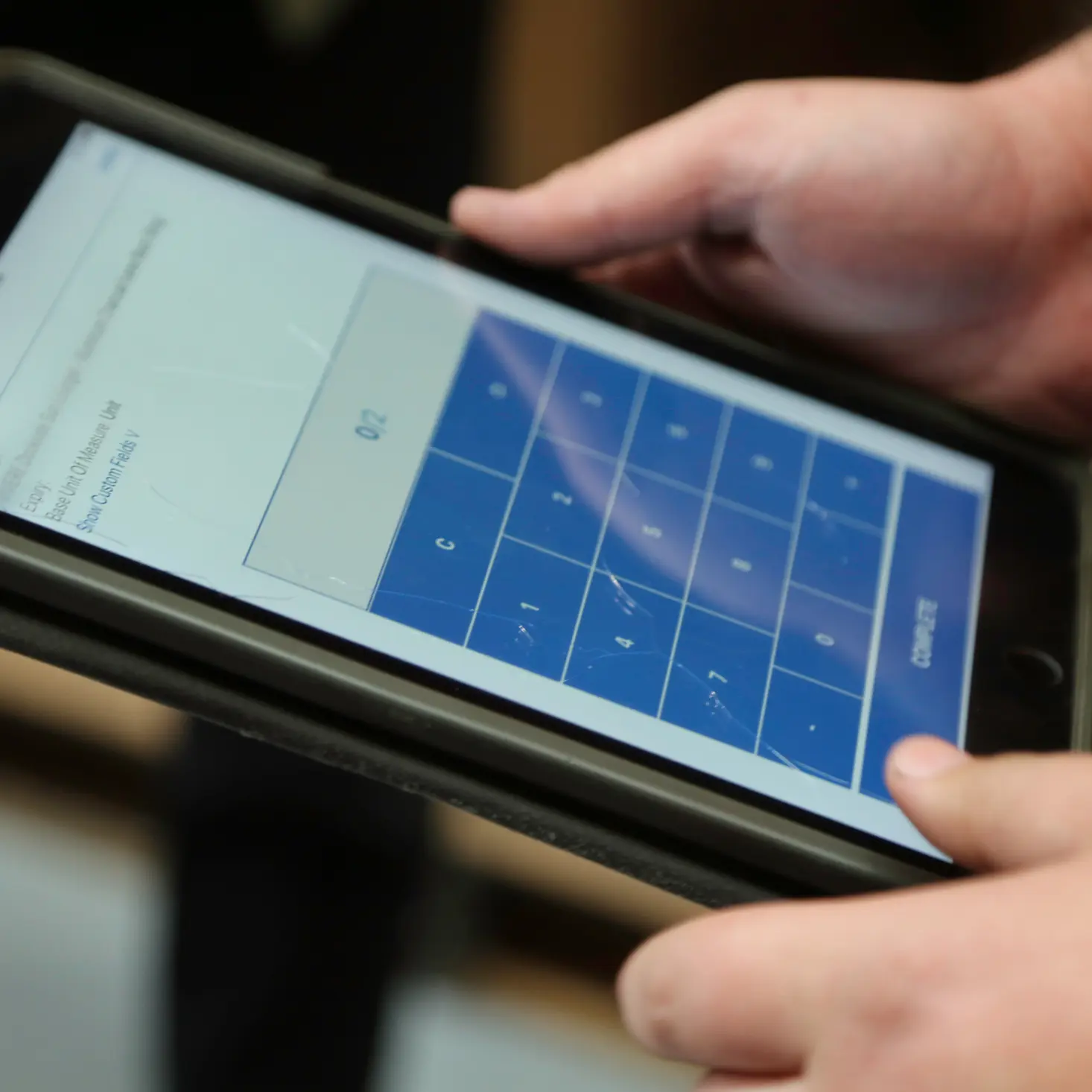 Close-up of hands holding a smartphone displaying a blue numeric keypad on the screen.