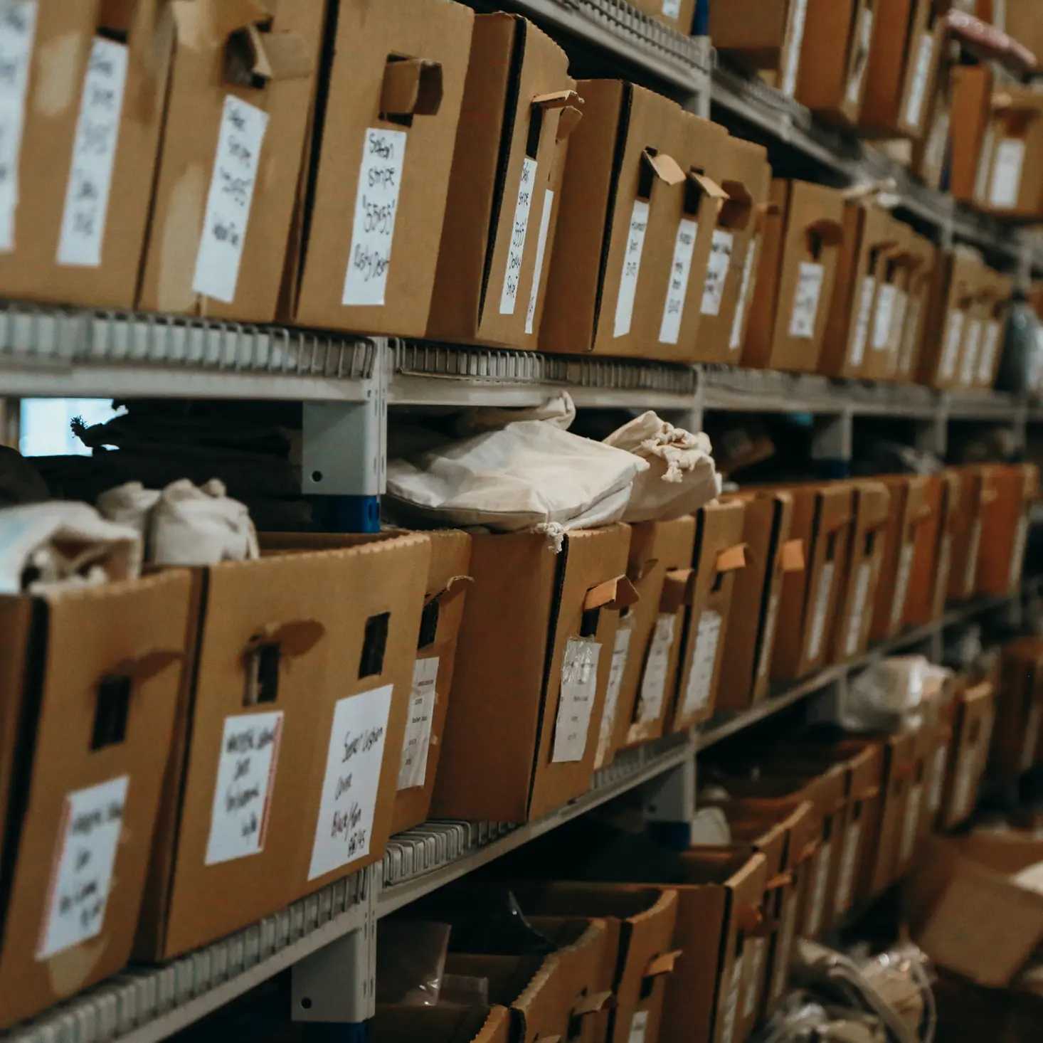 Shelves filled with cardboard storage boxes and cloth bags in a warehouse.