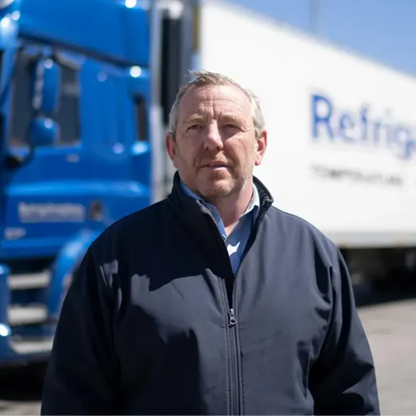 Paul Farnan National Operations Manager at Refrigafreighters standing in front of a blue truck and a refrigerated trailer.