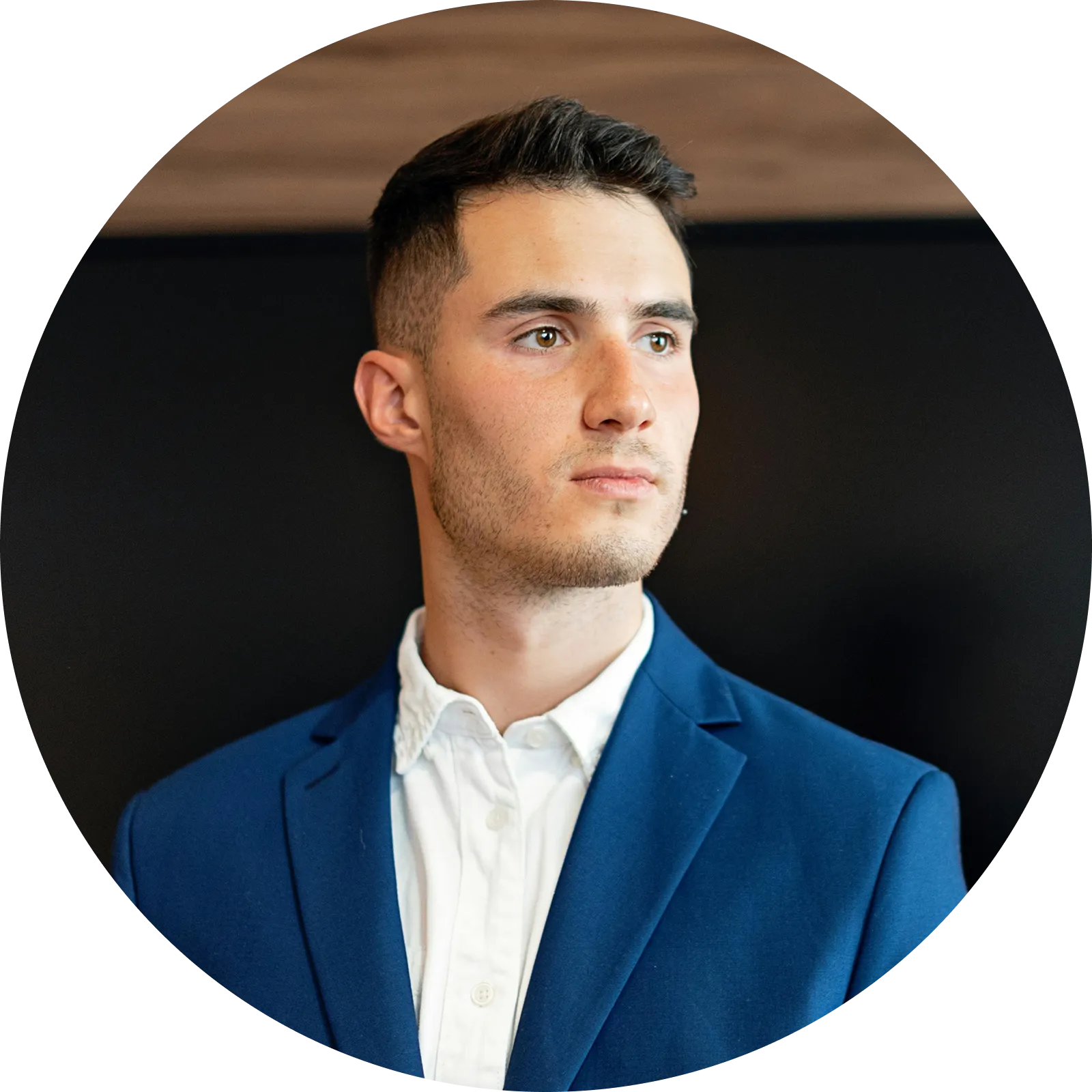 Portrait of a young man with short dark hair wearing a white shirt and blue blazer, looking to the side.