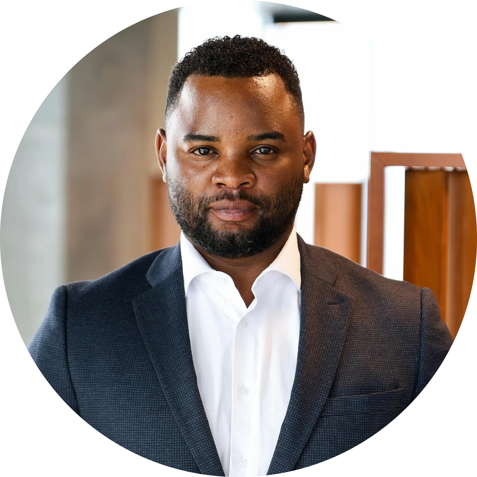 Professional man with short curly hair and beard, wearing a dark suit jacket and white shirt, looking directly at the camera.