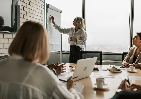 Woman presenting ideas on a flip chart during a business meeting with colleagues seated around a table.