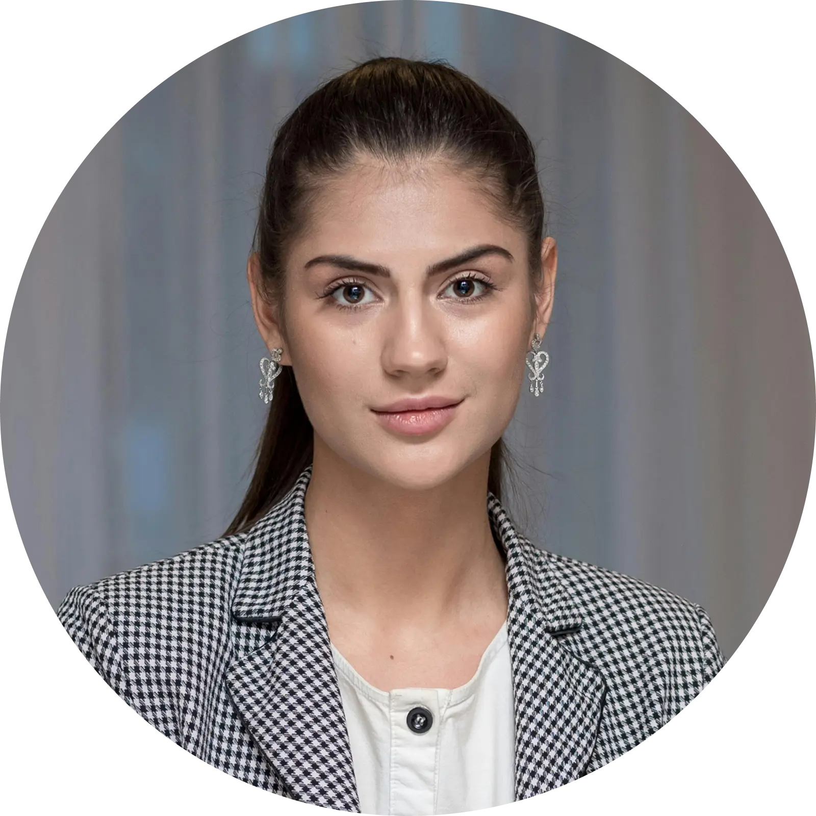 Portrait of a young woman with dark hair in a ponytail, wearing a houndstooth blazer and silver earrings.