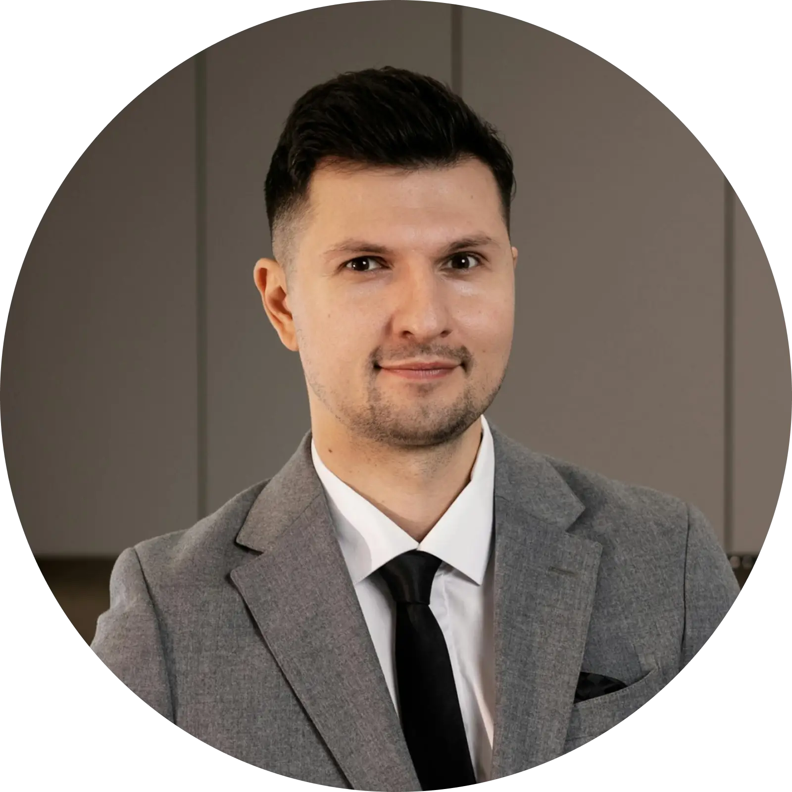 Smiling man with short dark hair wearing a gray suit, white shirt, and black tie against a neutral background.