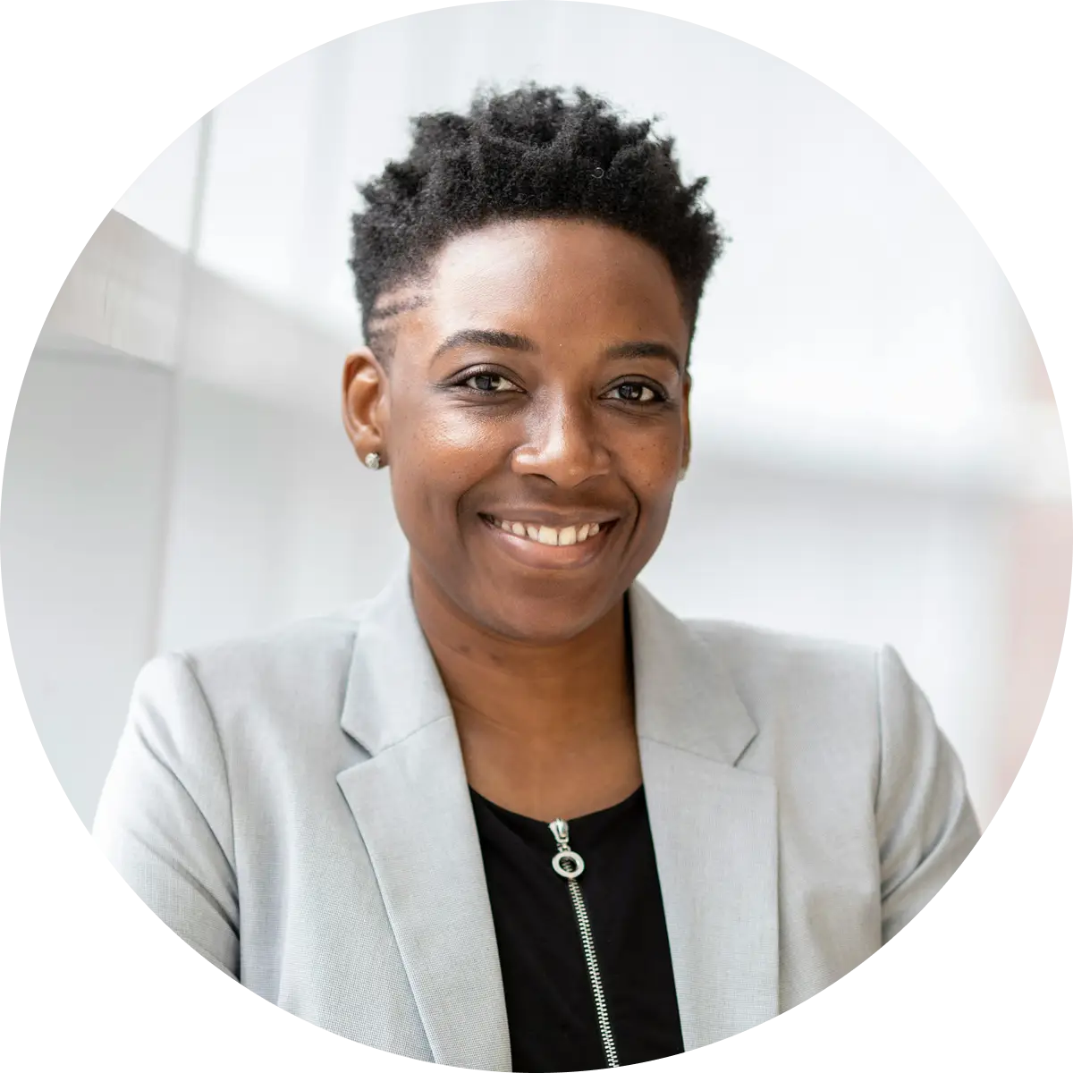 Smiling woman with short curly hair wearing a light gray blazer and black top with zipper.