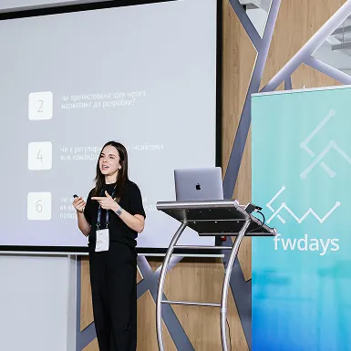 Жінка проводить презентацію на конференції FWDAYS біля екрана та стенда з логотипом заходу.