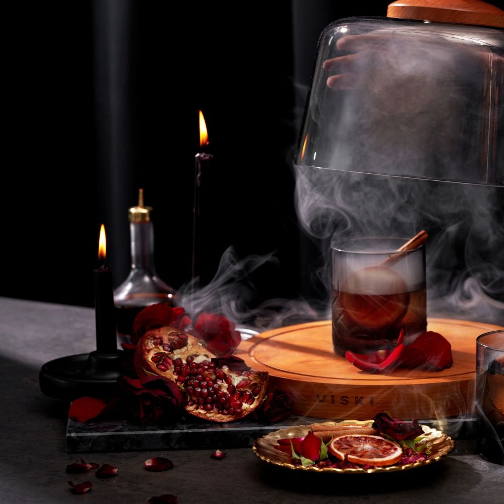 A smoked cocktail under a glass cloche on a dark bar, with Viski barware