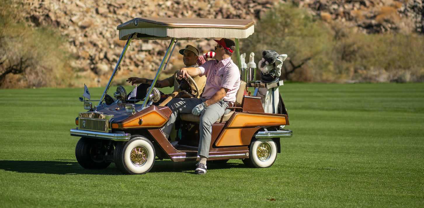 Two golfers in Nation Golf Co. apparel driving a vintage golf cart on the course