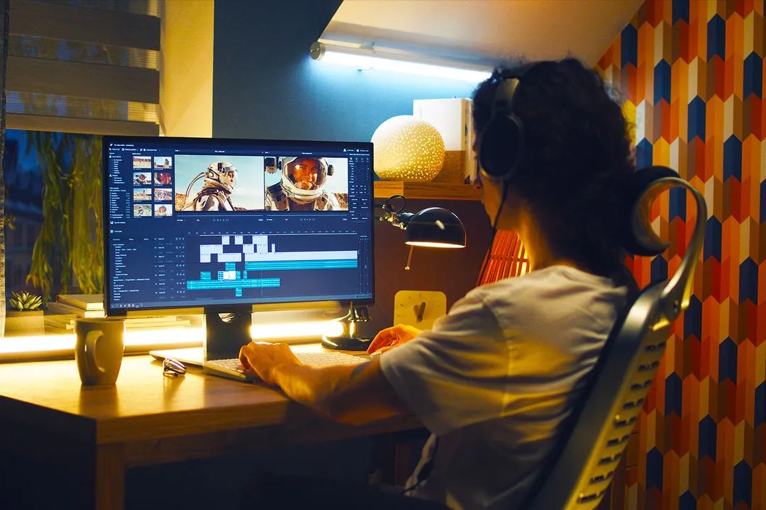 Joven sentado frente a una computadora editando el programa de edición DaVinci Resolve. la habitación tiene un luz cálida y acogedora.