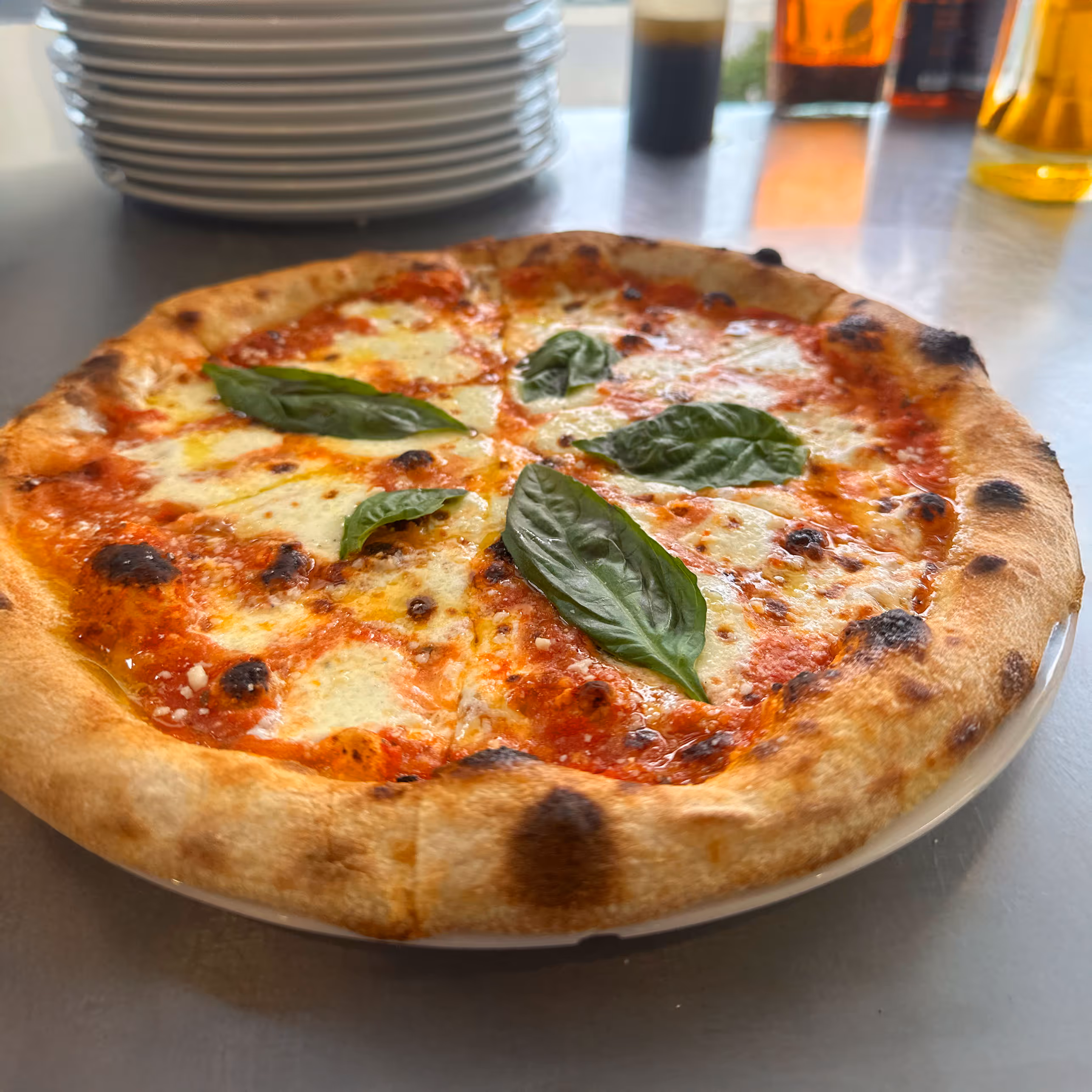 Close-up of a freshly baked pizza margherita with melted mozzarella, vibrant tomato sauce, and basil leaves, set atop a stack of white plates.