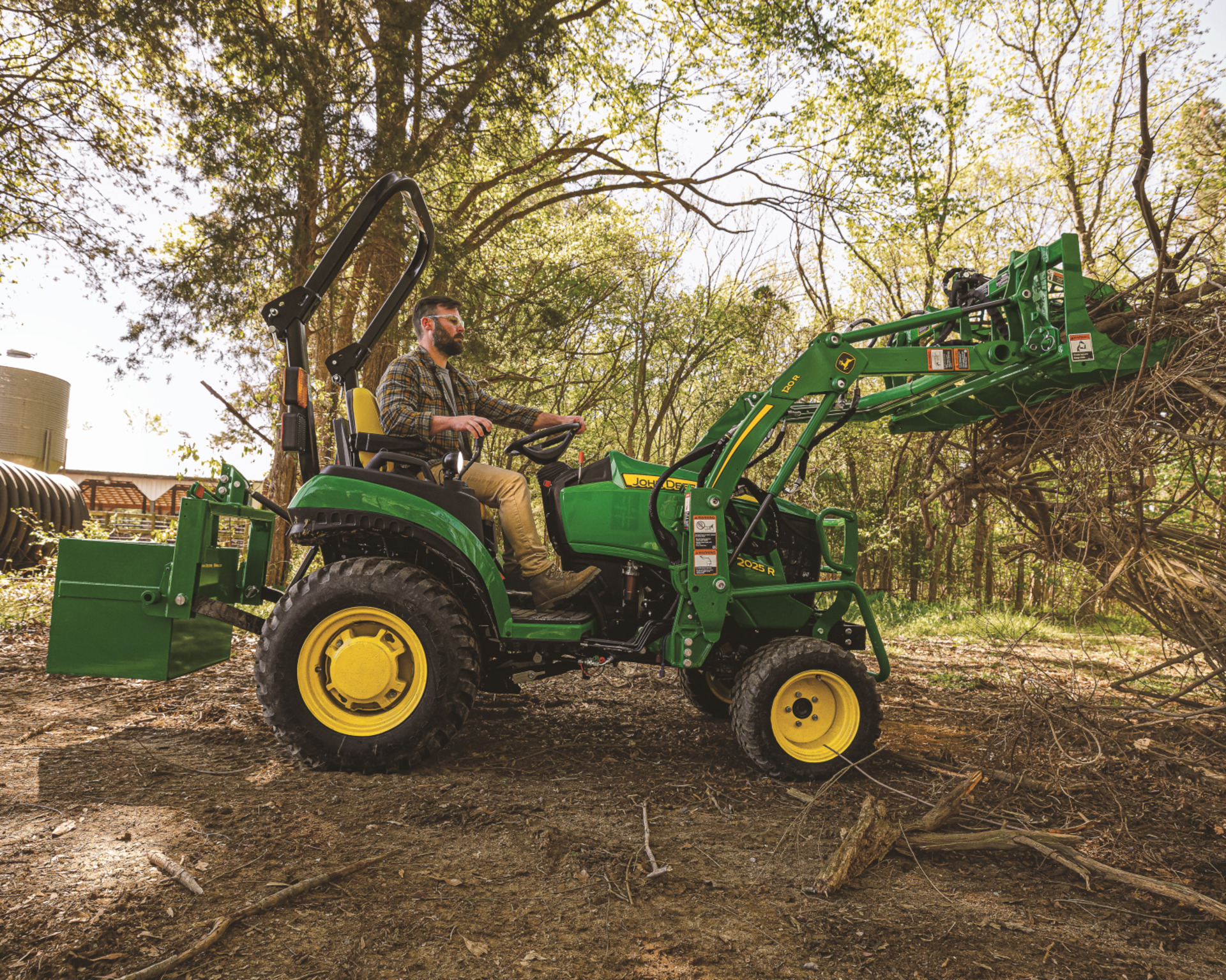 A property manager uses a John Deere compact tractor with attachments to clear brush.