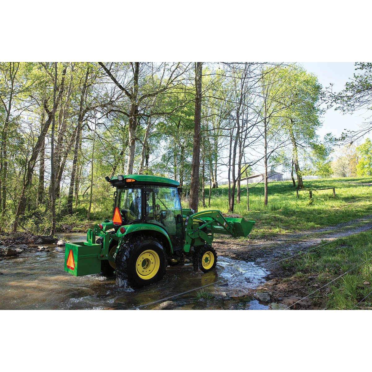 Side right view of a 3046R compact utility tractor crossing a stream in a wooded area