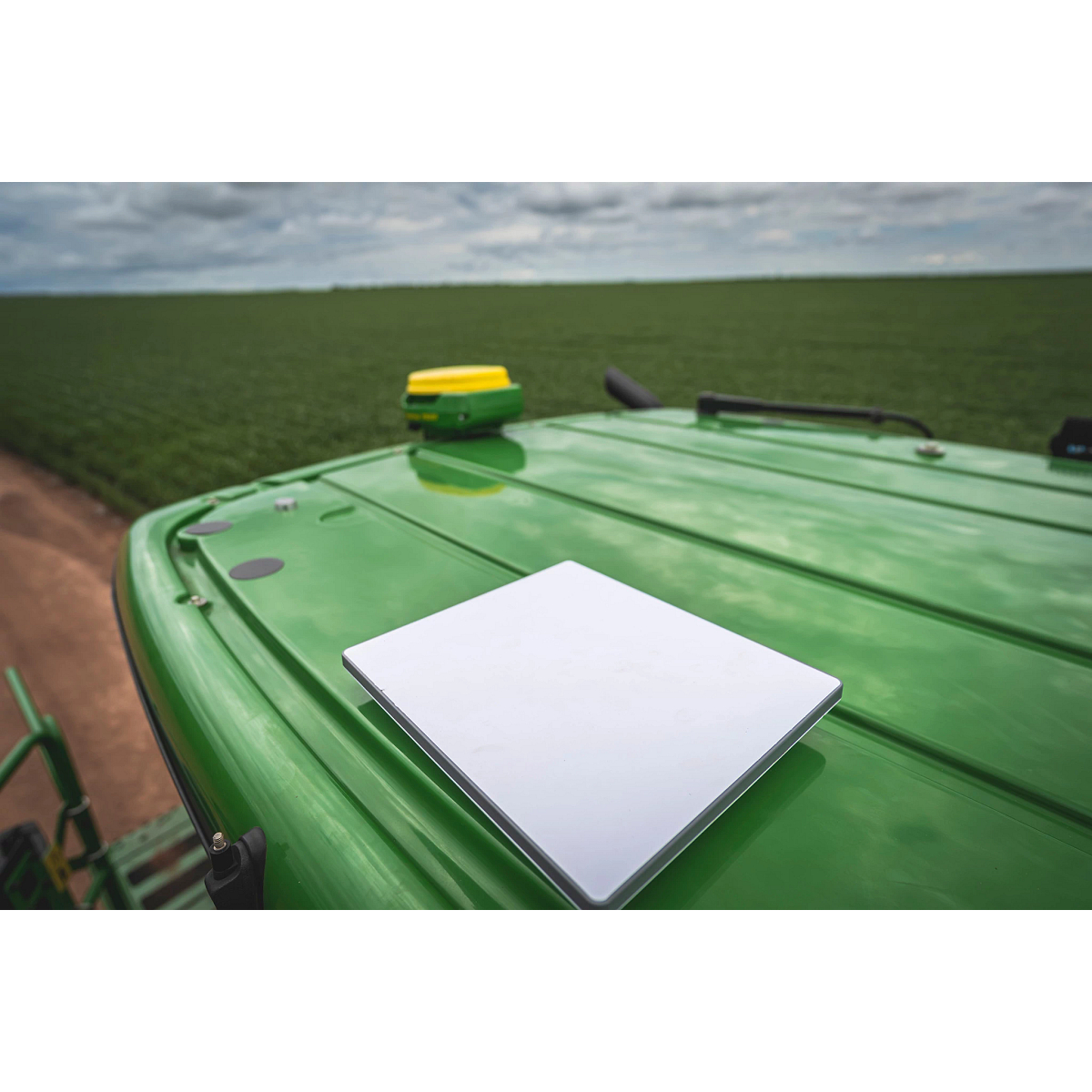 JDLink Boost Mini Terminal mounted on the roof of a green John Deere machine, shown from the back with an agricultural field visible in the background.