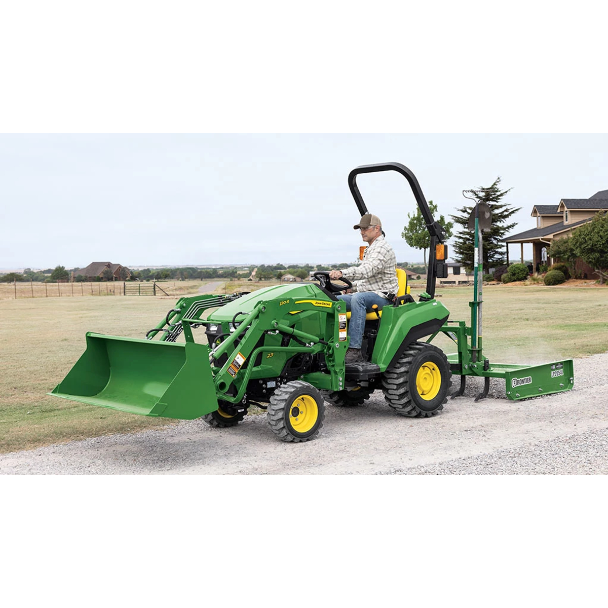 A person driving a green compact tractor equipped with a loader and land plane spreading gravel on a gravel road.