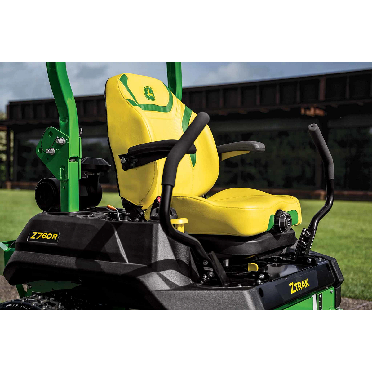 A zoomed-in shot of a yellow zero-turn mower seat with green detailing in front of a commercial building.