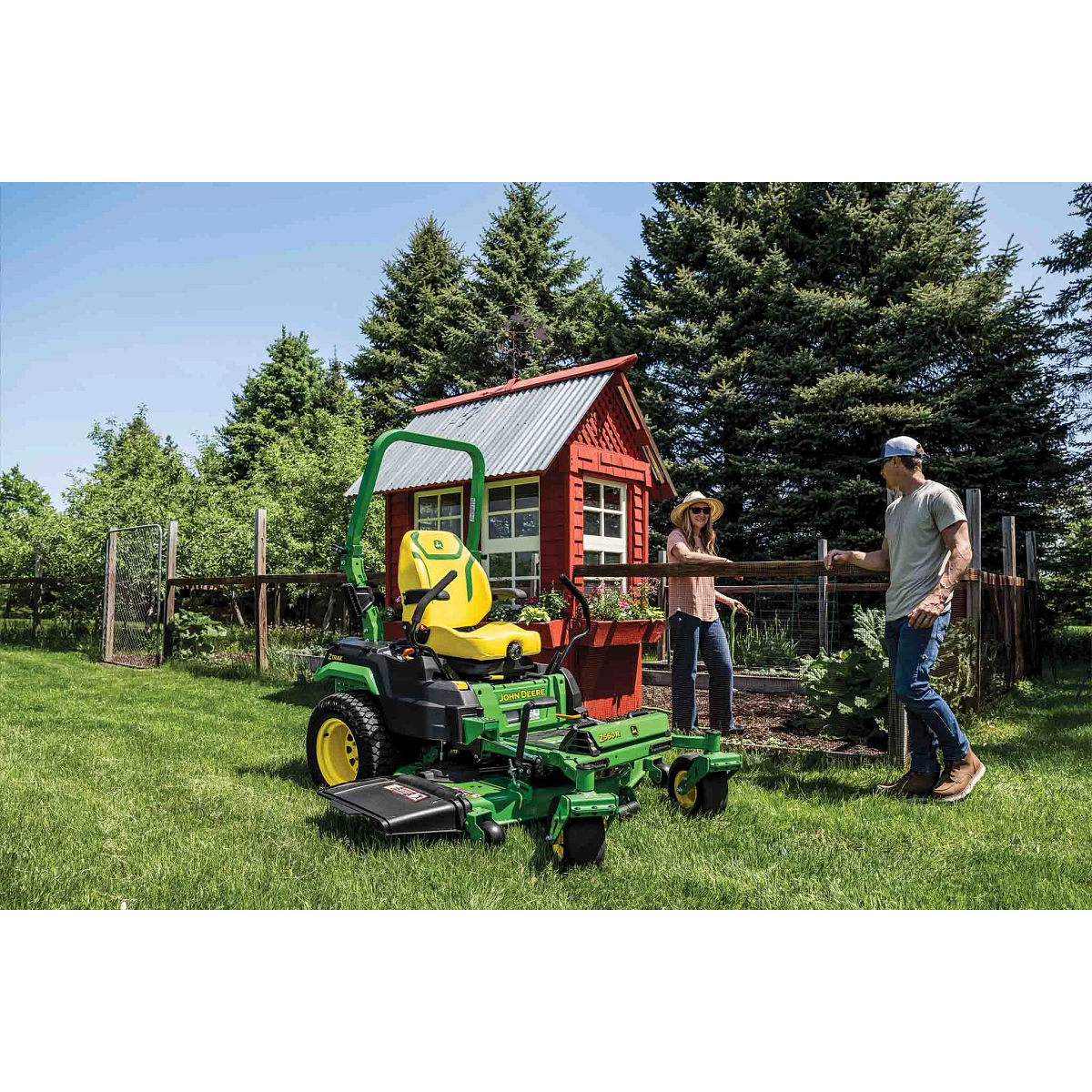 A Z560R zero-turn mower rests on a well-kept lawn next to two people chatting near fenced-in garden.