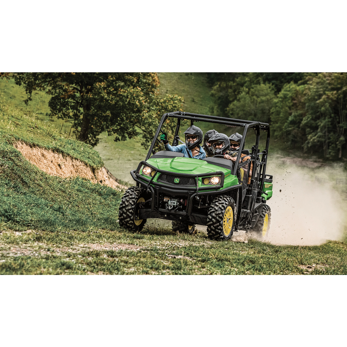 Front left view of an XUV 590M S4 Gator with four helmeted passengers tearing down a grassy path, dust flying behind it