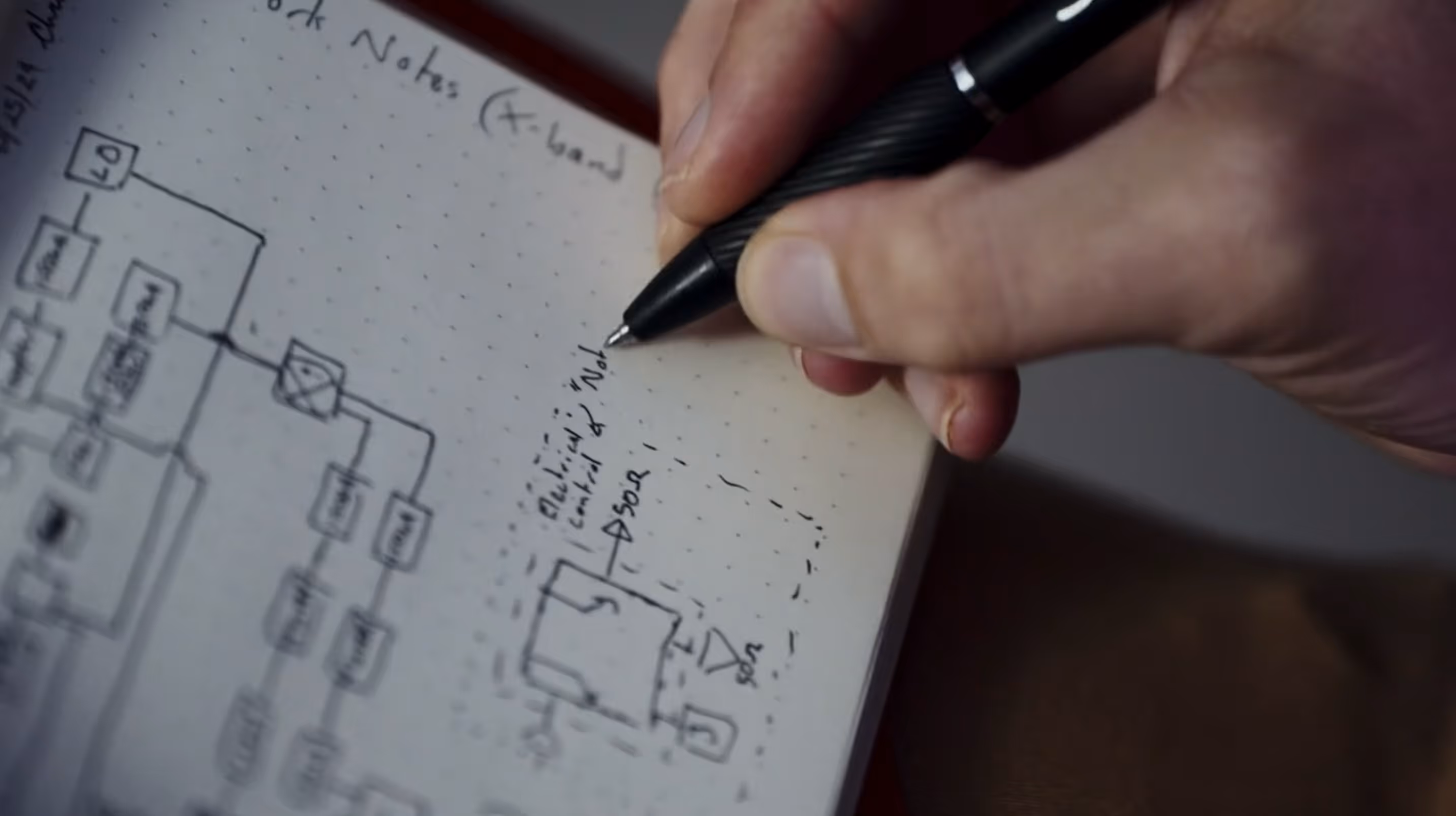 Hand holding a pen sketching an electrical control diagram on dotted paper.