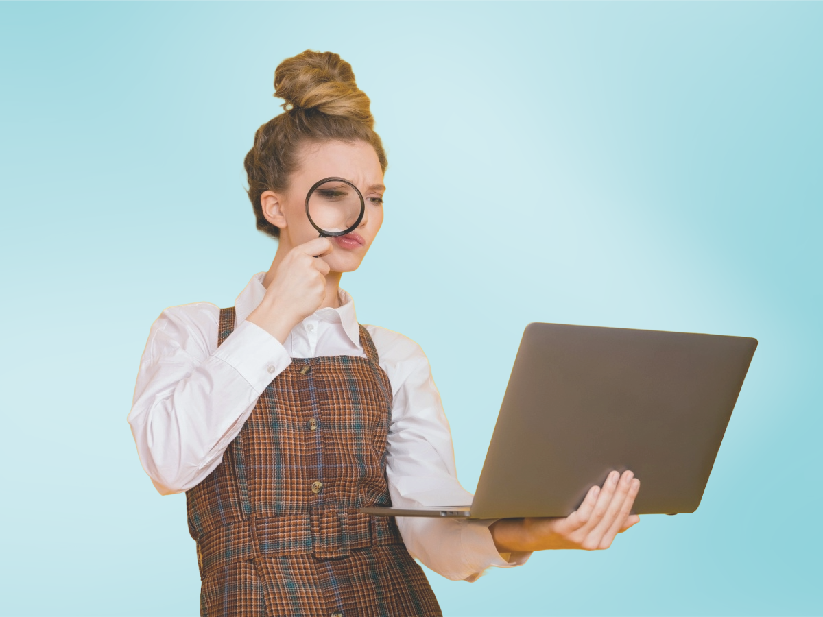 Femme tenant un ordinateur portable dans une main et observant l'écran avec une loupe, sur fond bleu clair.
