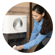 Woman in blue shirt handling a component inside a white appliance with a circular vent.