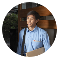 Smiling young man in a blue shirt holding a package and carrying a shoulder bag.