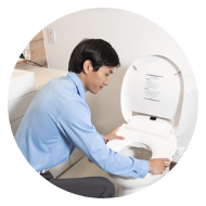 Man wearing a blue shirt cleaning the inside of a white toilet bowl.