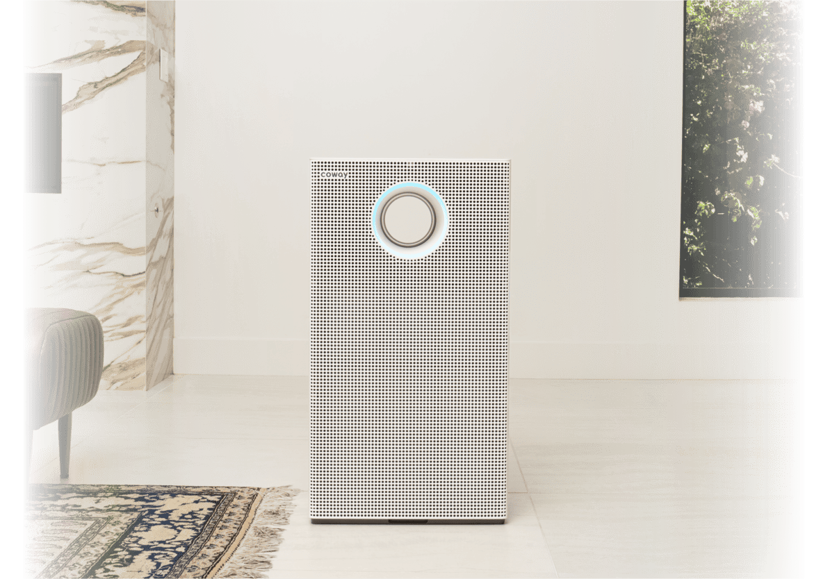 Coway AP-1523D air purifier with a circular control on the front, placed on a tiled floor near a patterned rug and marble wall.